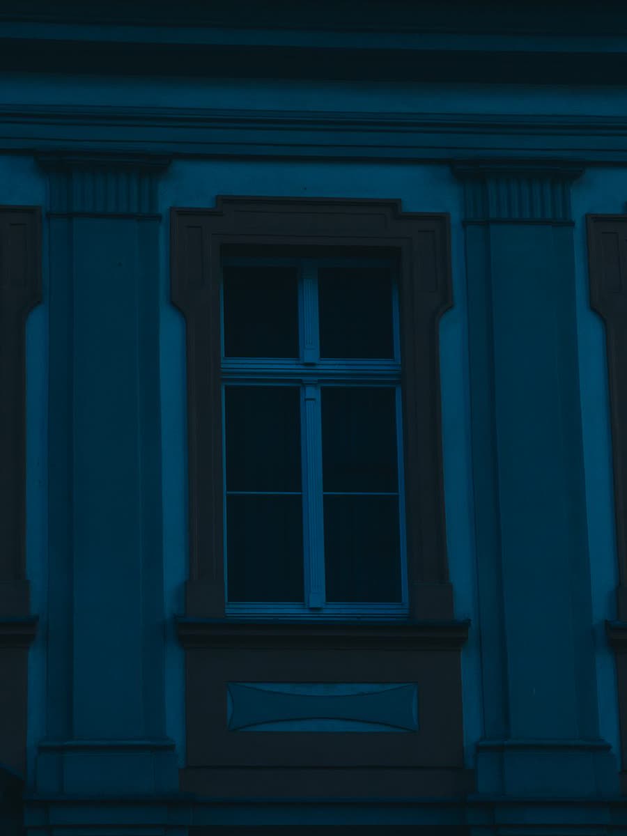 Ett upplyst fönster i en mörkblå fasad i kvällsljus.